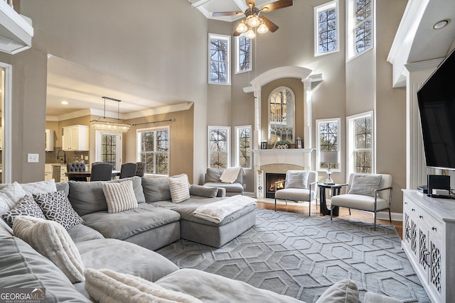 living area featuring ceiling fan, light wood-style flooring, baseboards, a lit fireplace, and crown molding