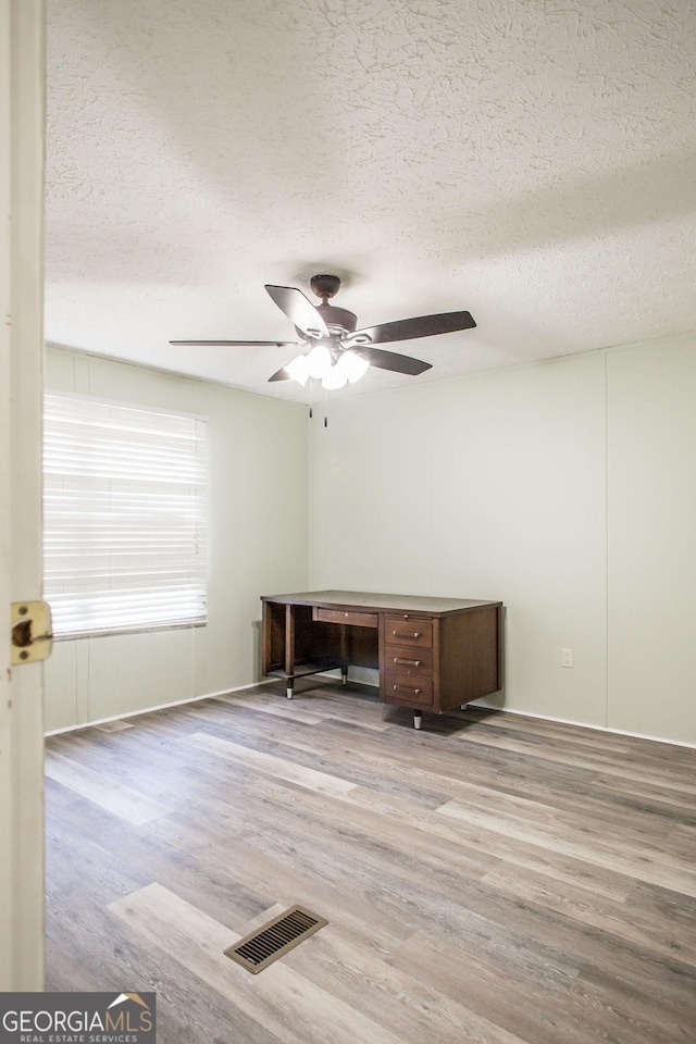 unfurnished office featuring ceiling fan, hardwood / wood-style floors, and a textured ceiling