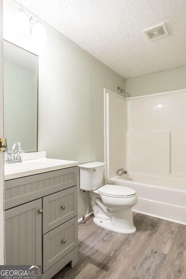 full bathroom with shower / bath combination, vanity, wood-type flooring, a textured ceiling, and toilet