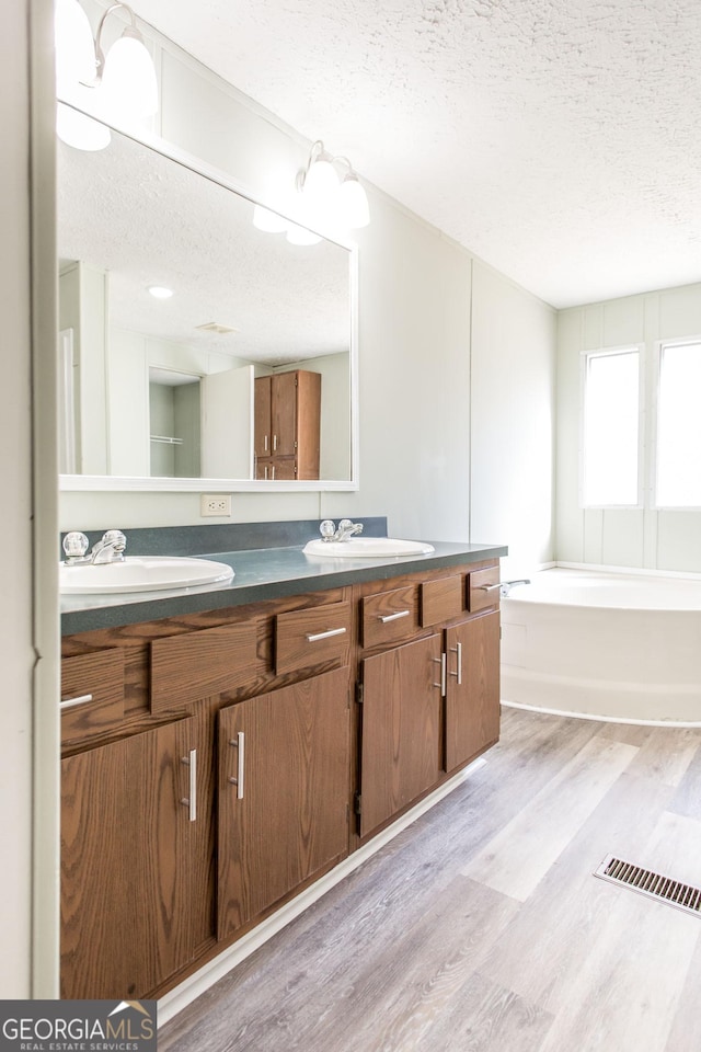 bathroom featuring a tub to relax in, wood-type flooring, a textured ceiling, and vanity