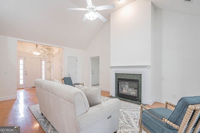 living room with ceiling fan, light wood-type flooring, high vaulted ceiling, and a tiled fireplace