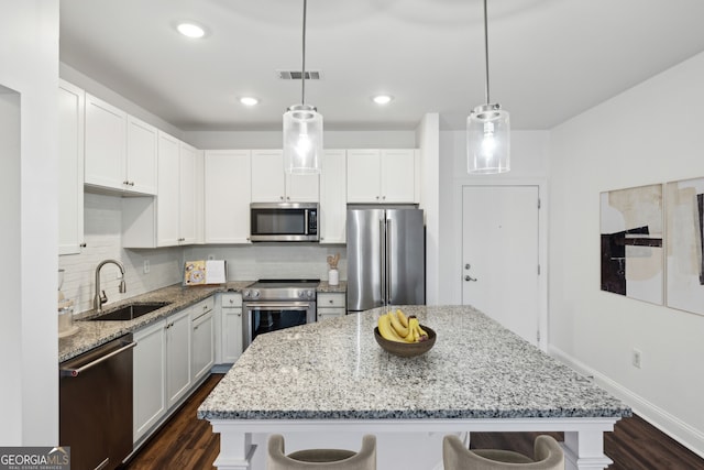 kitchen featuring pendant lighting, sink, appliances with stainless steel finishes, a center island, and a kitchen bar