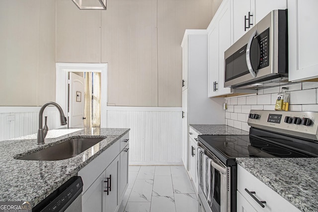 kitchen with marble finish floor, appliances with stainless steel finishes, white cabinets, a sink, and light stone countertops