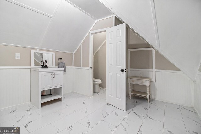 bathroom featuring marble finish floor, wainscoting, vaulted ceiling, and toilet