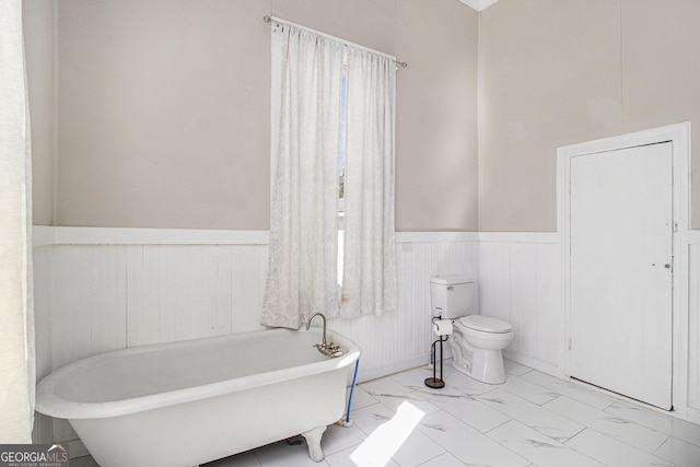 bathroom featuring marble finish floor, wainscoting, a freestanding tub, and toilet