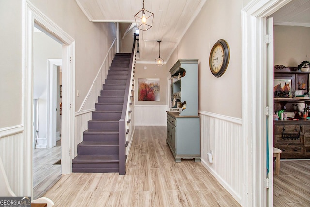 foyer entrance featuring a wainscoted wall, stairway, ornamental molding, and light wood-style floors