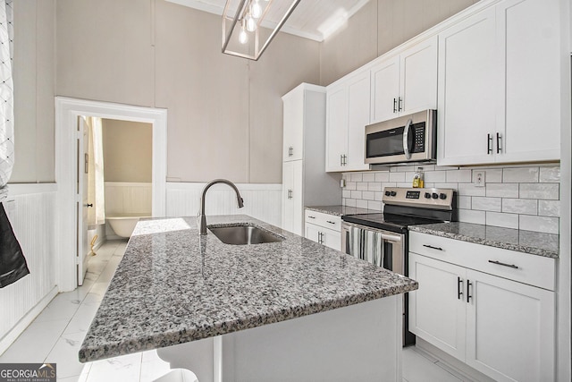 kitchen with dark stone counters, a kitchen island with sink, stainless steel appliances, white cabinetry, and a sink