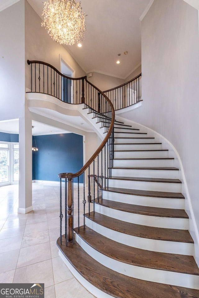 stairs with tile patterned flooring, ornamental molding, a towering ceiling, and an inviting chandelier