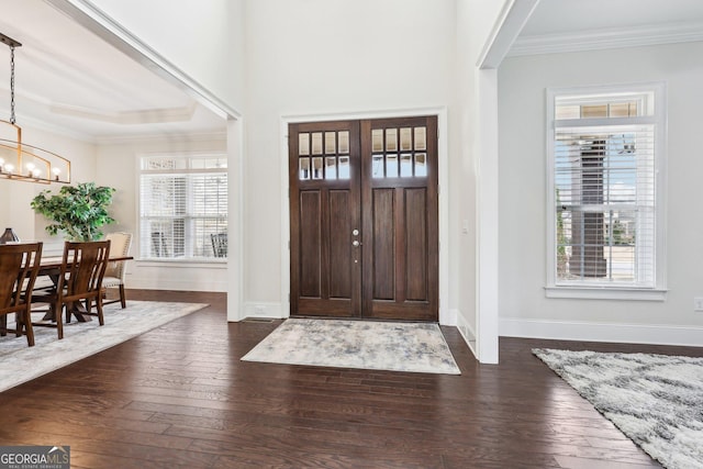 foyer with crown molding, dark wood-type flooring, and a chandelier