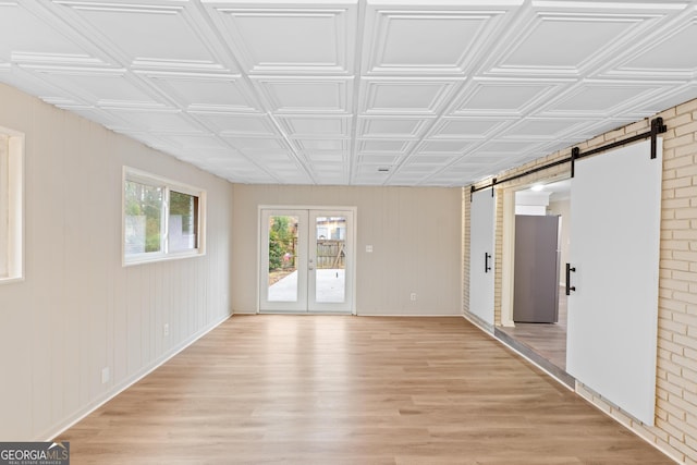 unfurnished room featuring light wood finished floors, french doors, a barn door, and an ornate ceiling