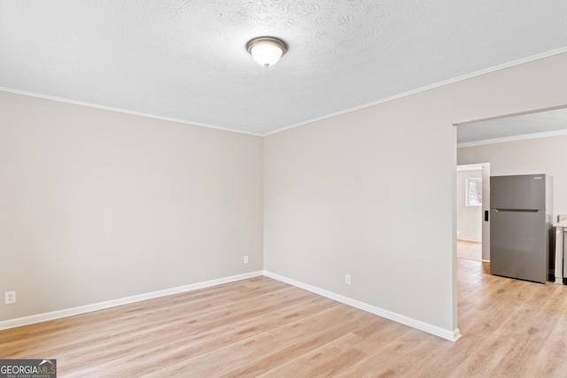 spare room with a textured ceiling, crown molding, light wood-type flooring, and baseboards