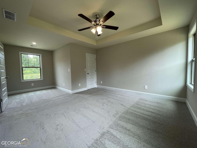 empty room with light carpet, visible vents, a tray ceiling, and baseboards