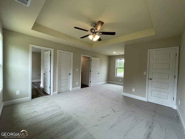 unfurnished bedroom with visible vents, baseboards, a raised ceiling, ensuite bath, and carpet floors