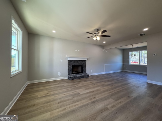 unfurnished living room with a stone fireplace, dark wood-style flooring, visible vents, and baseboards