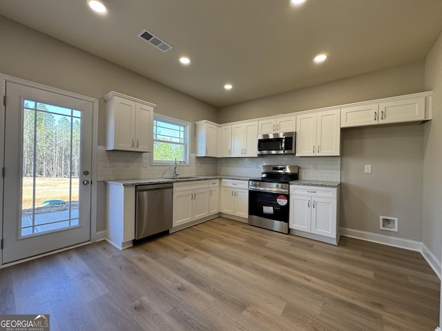 kitchen featuring stainless steel appliances, visible vents, light wood-style flooring, white cabinets, and a sink