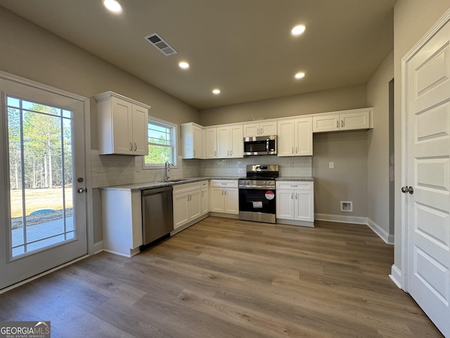 kitchen featuring stainless steel appliances, wood finished floors, a sink, visible vents, and white cabinets