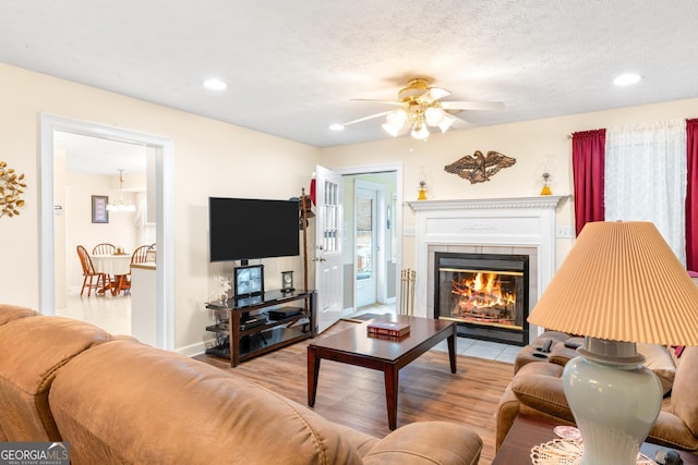 living area featuring baseboards, a ceiling fan, a fireplace with flush hearth, a textured ceiling, and recessed lighting