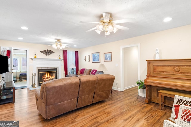 living area featuring light wood finished floors, a ceiling fan, a textured ceiling, a tile fireplace, and baseboards