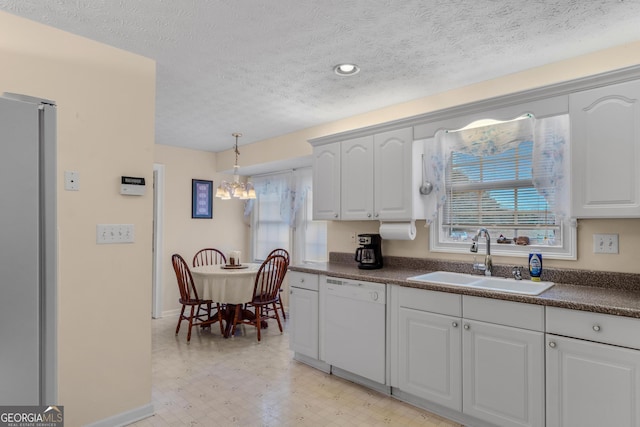 kitchen with dark countertops, freestanding refrigerator, dishwasher, and a sink