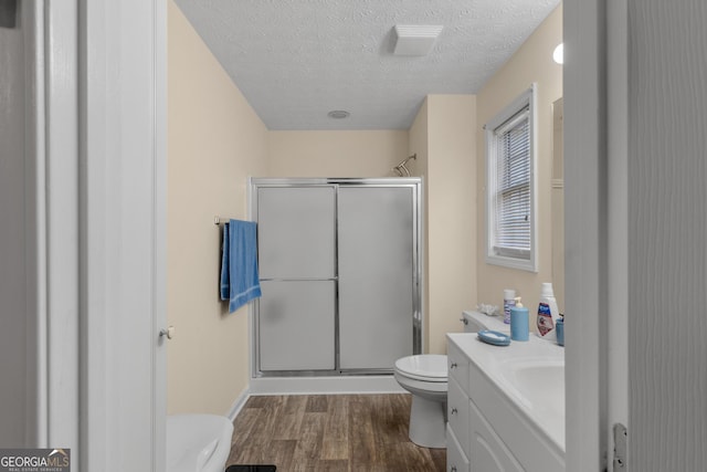 bathroom with a textured ceiling, toilet, wood finished floors, vanity, and a stall shower