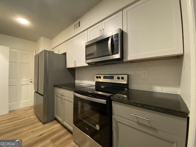 kitchen with appliances with stainless steel finishes, white cabinetry, light hardwood / wood-style floors, decorative backsplash, and dark stone counters