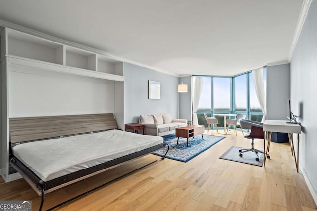 bedroom with crown molding, a wall of windows, a water view, and light wood-type flooring