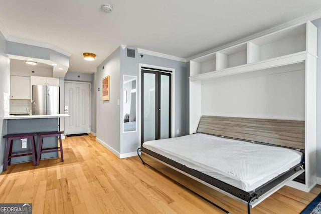 bedroom with crown molding, stainless steel refrigerator, and light hardwood / wood-style floors