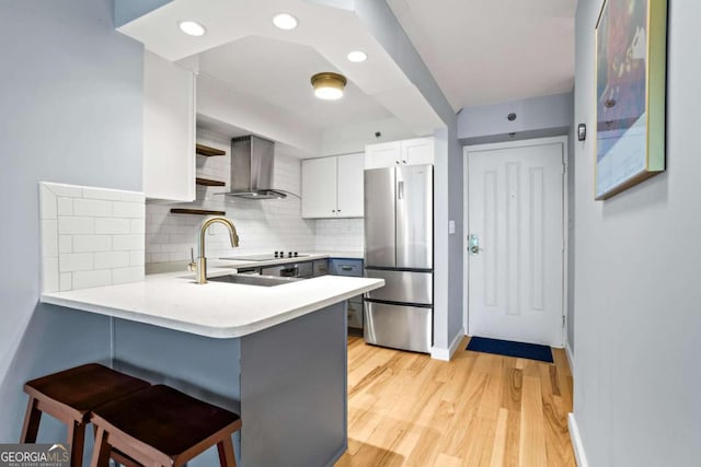 kitchen featuring stainless steel refrigerator, a breakfast bar, white cabinets, kitchen peninsula, and wall chimney exhaust hood