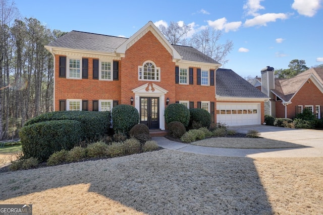 colonial house with driveway, brick siding, and french doors