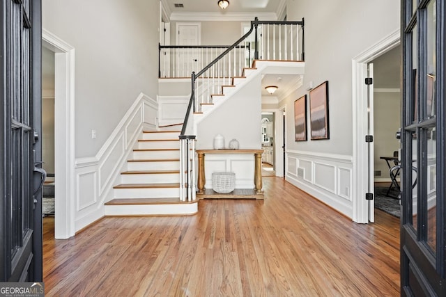 foyer with crown molding, wood finished floors, stairs, and a decorative wall