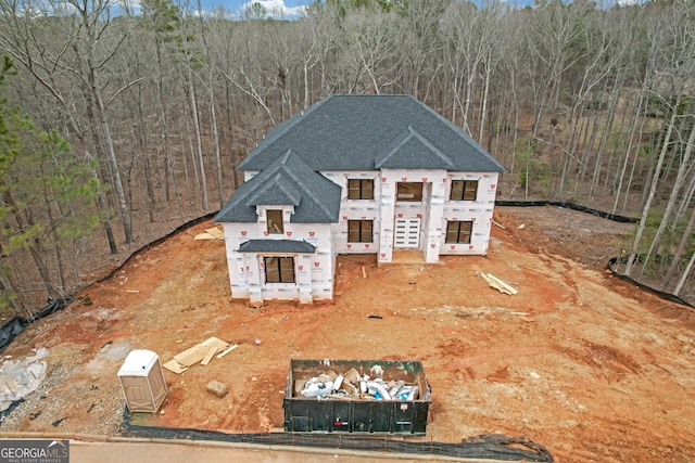 view of front of house with a view of trees and roof with shingles