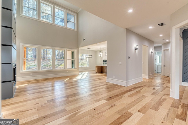 unfurnished living room featuring a towering ceiling and light hardwood / wood-style flooring