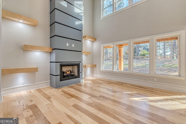 unfurnished living room featuring a multi sided fireplace, light hardwood / wood-style floors, and a high ceiling