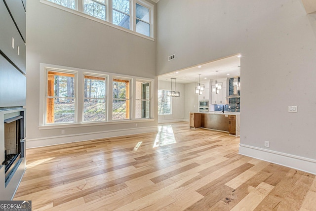 unfurnished living room featuring a towering ceiling, sink, light wood-type flooring, a brick fireplace, and an inviting chandelier