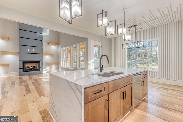 kitchen featuring pendant lighting, sink, dishwasher, a kitchen island with sink, and light stone counters