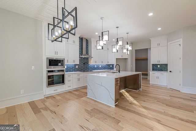 kitchen with appliances with stainless steel finishes, pendant lighting, white cabinets, light stone countertops, and a center island with sink