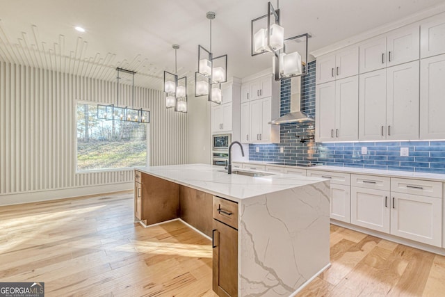 kitchen with white cabinetry, hanging light fixtures, sink, and a center island with sink