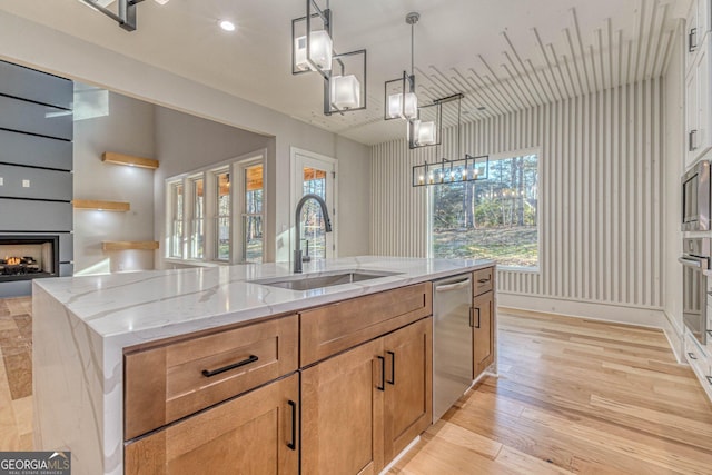 kitchen featuring appliances with stainless steel finishes, an island with sink, sink, hanging light fixtures, and light stone counters