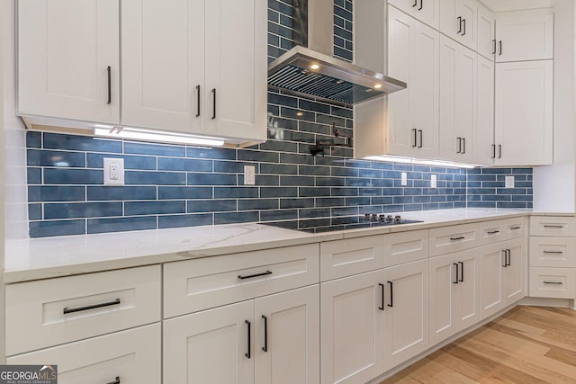 kitchen with white cabinets, light hardwood / wood-style floors, light stone countertops, wall chimney range hood, and black electric cooktop