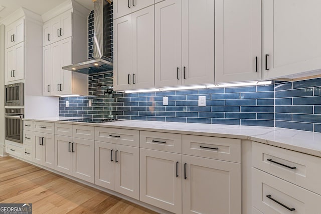 kitchen featuring white cabinetry, light stone counters, appliances with stainless steel finishes, light hardwood / wood-style floors, and wall chimney range hood