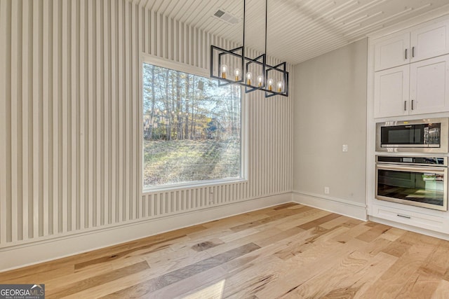 unfurnished dining area featuring a notable chandelier, light hardwood / wood-style flooring, and a wealth of natural light