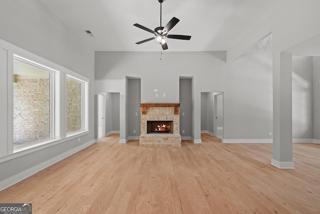 unfurnished living room with ceiling fan, a fireplace, light hardwood / wood-style flooring, and a high ceiling