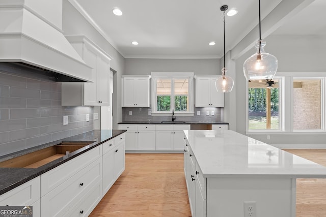 kitchen featuring a kitchen island, sink, white cabinets, dark stone counters, and custom range hood