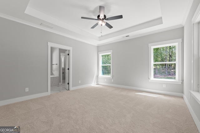 unfurnished bedroom with ornamental molding, light carpet, ensuite bath, and a tray ceiling