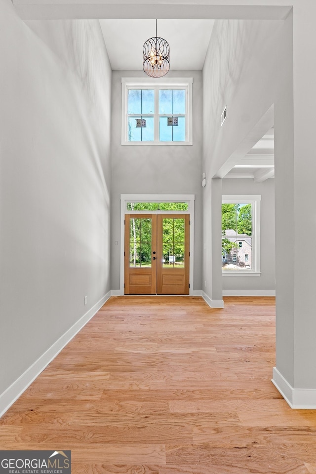 entryway with french doors, a towering ceiling, a chandelier, and light hardwood / wood-style floors