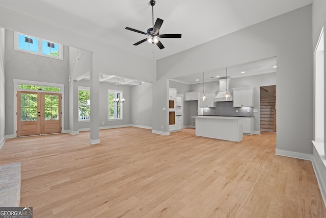 unfurnished living room with a high ceiling, ceiling fan with notable chandelier, light wood-type flooring, and french doors