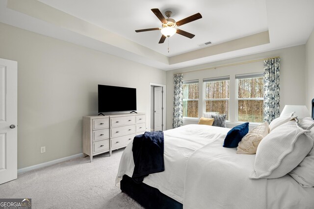 carpeted bedroom featuring a tray ceiling and ceiling fan