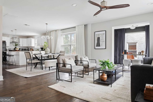 living room with ceiling fan with notable chandelier and dark hardwood / wood-style flooring