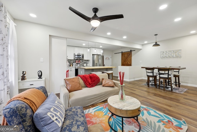 living room with a barn door, hardwood / wood-style floors, and ceiling fan