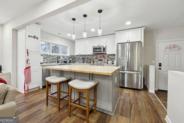 kitchen featuring appliances with stainless steel finishes, butcher block counters, hanging light fixtures, and white cabinets